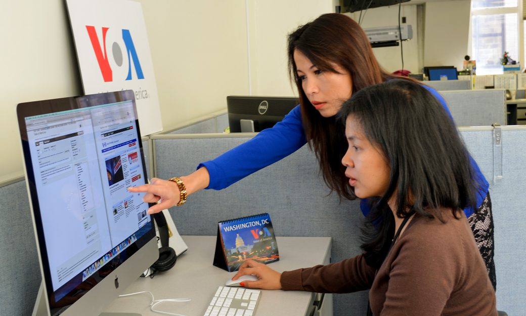 Two Asian women work in front of a computer at a VOA office