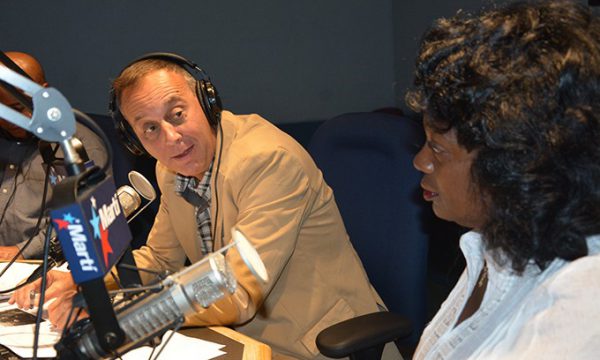 man in radio studio speaks into a mic while talking to woman