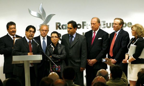 Group of people stand on a dias, one speaks into a microphone