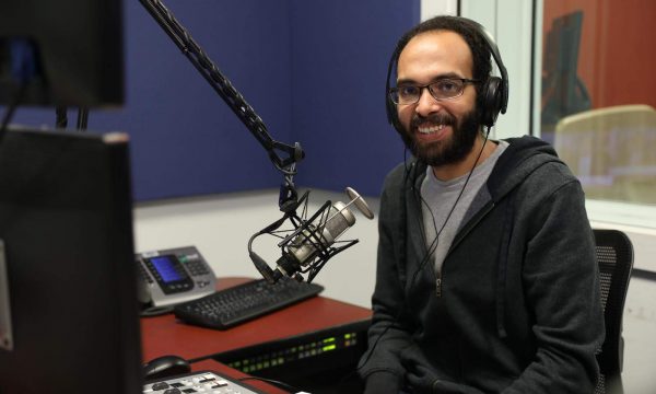bearded man wearing headphones and sitting next to a radio microphone